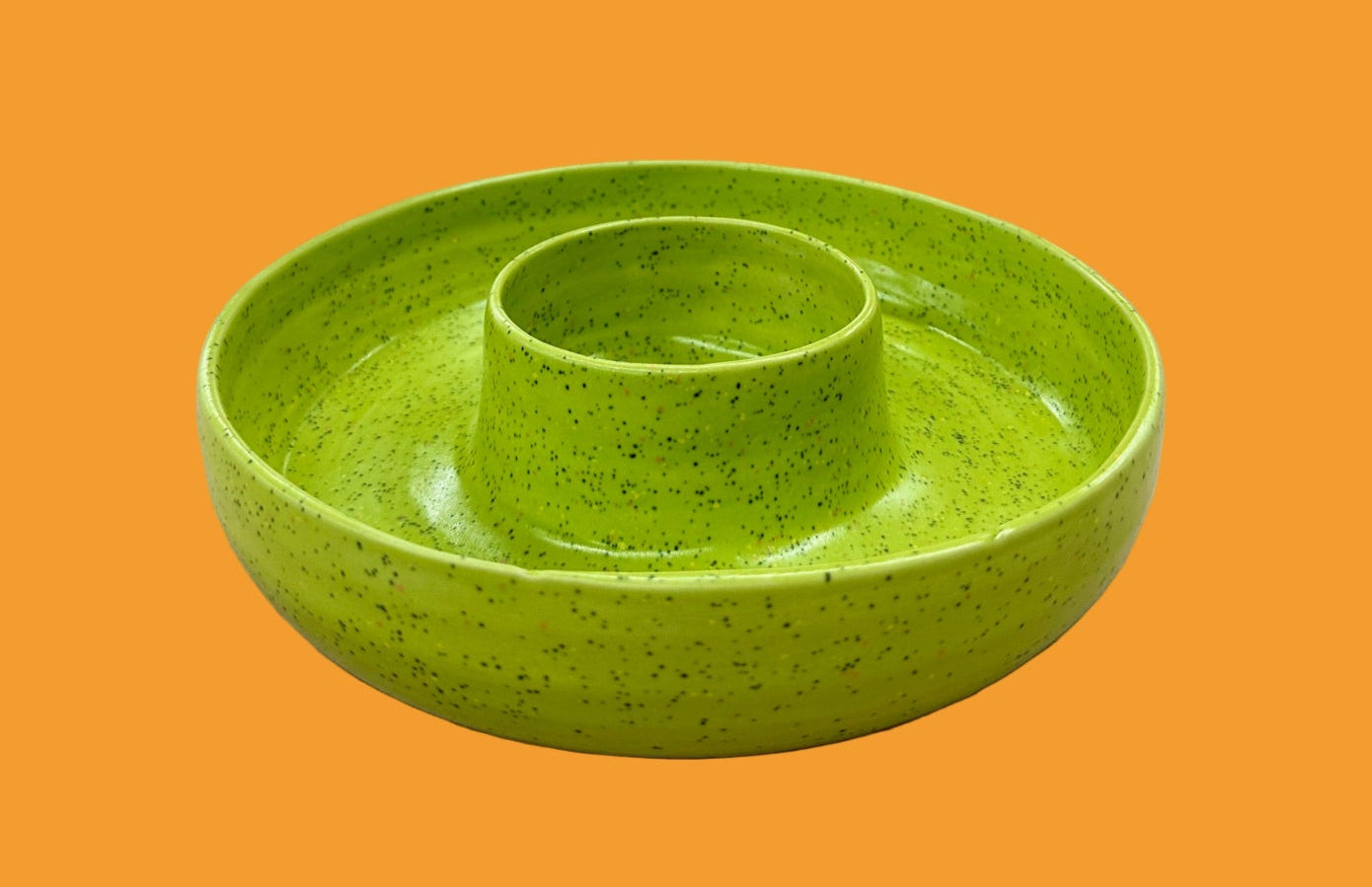 Green ceramic dish on a table with a vase of flowers in the background